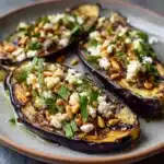 aubergines rôties garnies de feta émiettée et de pignons grillés sur assiette